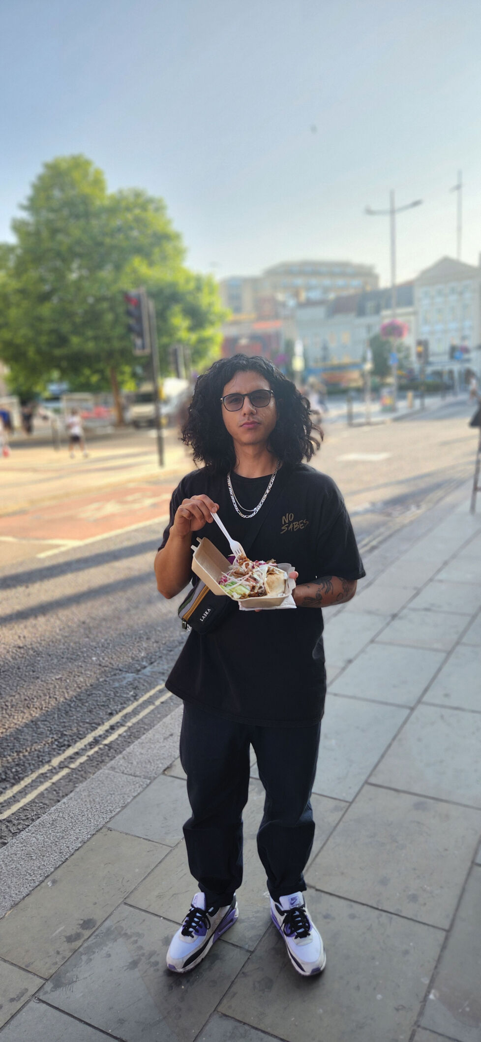 Charly Ortiz-Martinez eats his lunch on a sidewalk his back to an urban street